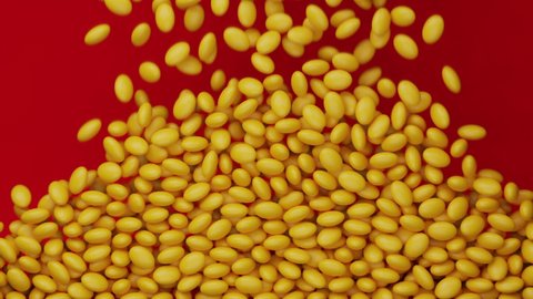 Bright and colorful candy beans or peanuts are falling down. Red background. Yellow colored tasty sugar sweets. Chocolate candies filling all the area. Close up. Holiday mood. 3D Render. 4K animation