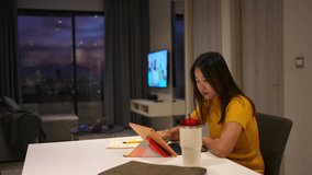 Asian woman using tablet with internet for online working on table in apartment at night. Female freelance type and scratch on tablet touch screen for business job plan or online shopping at home.