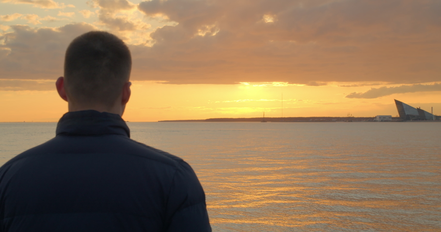 The man is enjoying the view of the golden sunset. The person feels relaxation, calmness and inner balance.