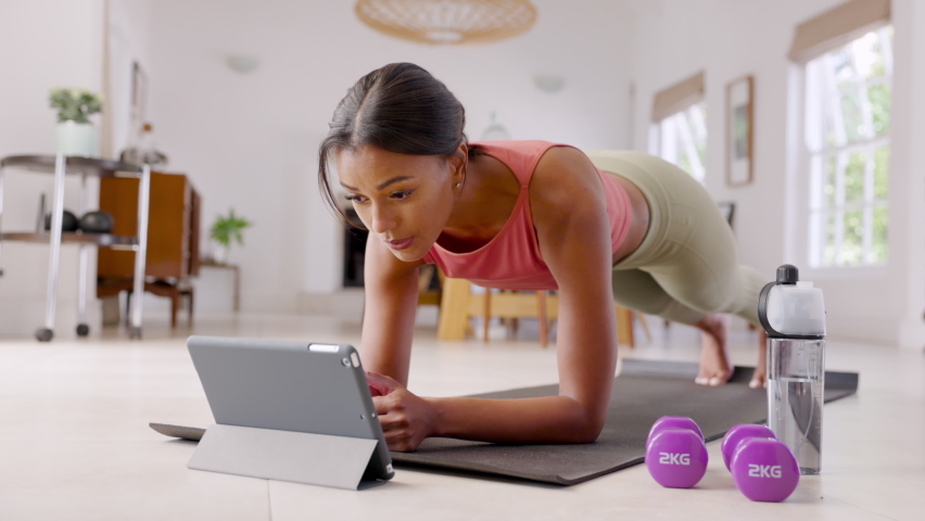 Mid adult fitness woman exercising at home and watching training videos on digital tablet. African american fit woman doing planks with a leg outstretched during online wokout. Royalty-Free Stock Footage #1073952956