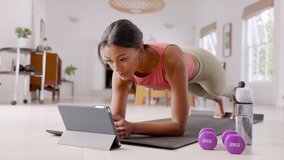 Mid adult fitness woman exercising at home and watching training videos on digital tablet. African american fit woman doing planks with a leg outstretched during online wokout.