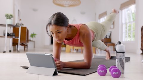Mid adult fitness woman exercising at home and watching training videos on digital tablet. African american fit woman doing planks with a leg outstretched during online wokout.