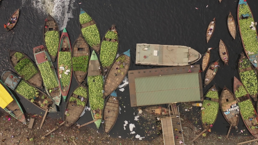 Aerial view of several small commercial boats with people unloading watermelons at Old Dhaka river port along Buriganga river in Dhaka, Bangladesh.