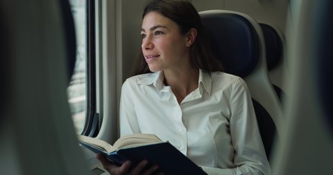 Cinematic shot of young business woman relaxing by reading book while travel by train for reach her destination for meeting. Concept: transportation, business and finance, education, travel, tourism.