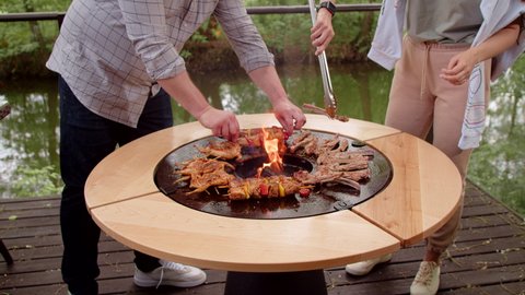 Meat on a round grill. We cook ribs and chicken tobacco on a designer grill. Guy and girl at the barbecue. Food on the grill close-up