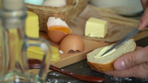 Close up of farmer male hands spread butter with knife on bread on background of rustic products eggs and cheese. Natural, healthy farm food.