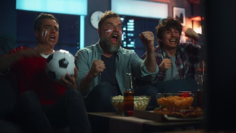 Night At Home: Three Joyful Soccer Fans on a Couch Watch Game on TV, Celebrate Victory when Sports Team Wins Championship. Friends Cheer for Favourite Football Club Play. Medium Shot