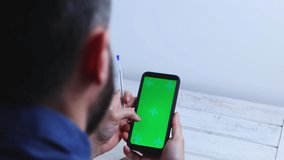 Man at home using Smartphone with Green Mock-up Screen, doing swiping, screen has tracking Markers