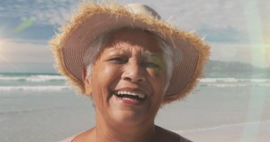 Animation of glowing light over senior woman smiling by seaside. retirement and happy senior life concept digitally generated video.