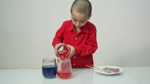 A boy with a skinhead hair and wearing a red long-sleeved shirt, 
proud of the mix of colors, embraces the glass jar with his hands.