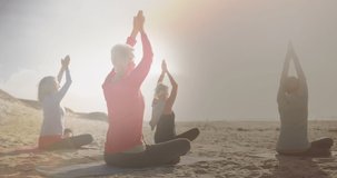 Animation of glowing light over happy senior women practicing yoga by seaside. retirement and senior life concept digitally generated video.
