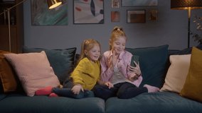 Happy little childrens girls making facetime video call with smartphone at home, using zoom meeting online app chat, social distancing communication remotely concept. Evening cozy apartment