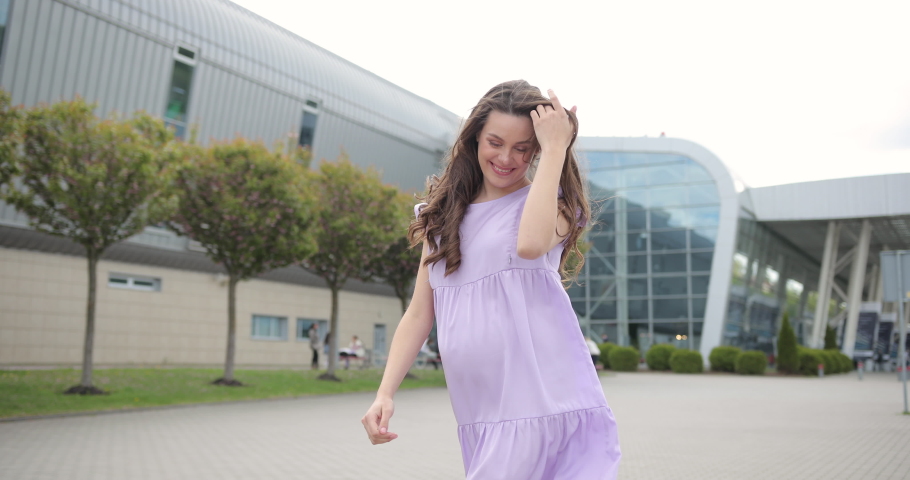 Beautiful young woman is pregnant and feels happy. Happy pregnant woman in a purple maternity dress walks around the city