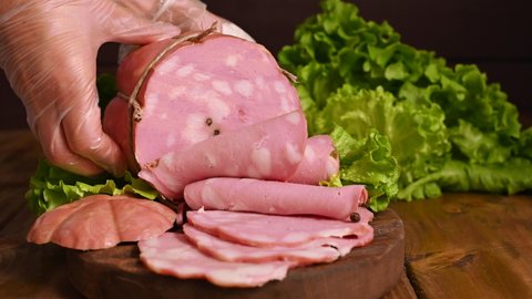 Mortadella. Large mortadella with pistachios on a wooden table. A man cuts thin slices of sausage. Traditional meat food in the Emilia Romagna region in Italy and in the city of Bologna. 4k footage