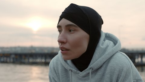 Portrait of beautiful muslim woman with piercing in nose breathing hard after morning jogging on street. Fitness active runner wearing sport clothes and hijab.