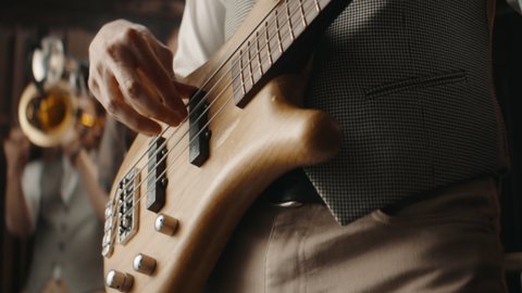 CU on hands, Caucasian male playing bass guitar during jazz band rehearsal in recording studio. Shot with 2x anamorphic lens