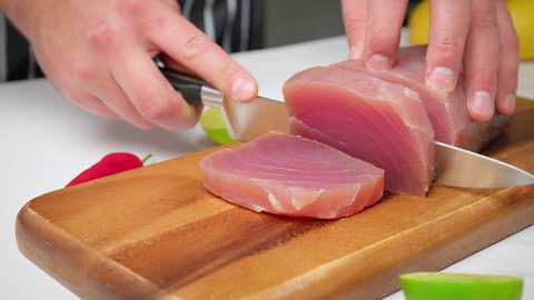 A chef's hands slicing raw tuna yellowfin on a table into a big steak size in 4K. Healthy meat, fresh tuna being cut in pieces on a chopping board for a tuna steak.