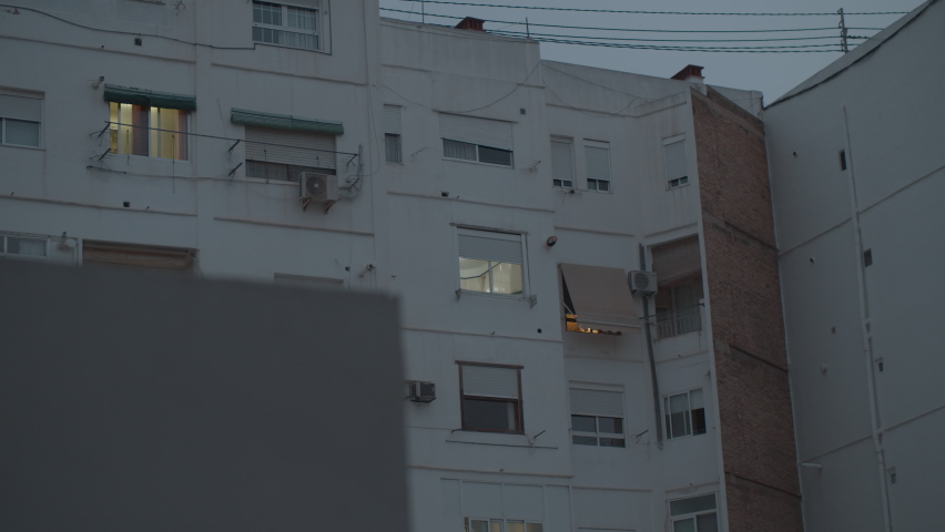 Evening view of apartment house. Many windows closed with shutters and just few with light