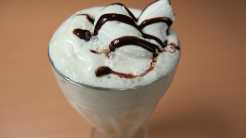 Close-up of vanilla milkshake with chocolate syrup on wooden table. Creamy milkshake decorated with chocolate above wooden surface. Refreshing desserts