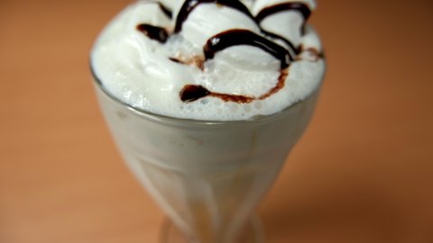 Close-up of vanilla milkshake with chocolate syrup on wooden table. Creamy milkshake decorated with chocolate above wooden surface. Refreshing desserts