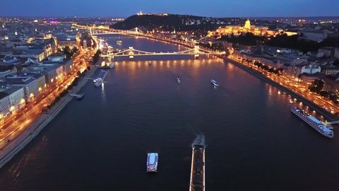 Cinematic 4K aerial drone night dolly shot of river cruise ships, Castle Hill, Buda Castle, Gellért Hill and the Citadella with the Danube river, bridges illuminated after sunset in Budapest, Hungary