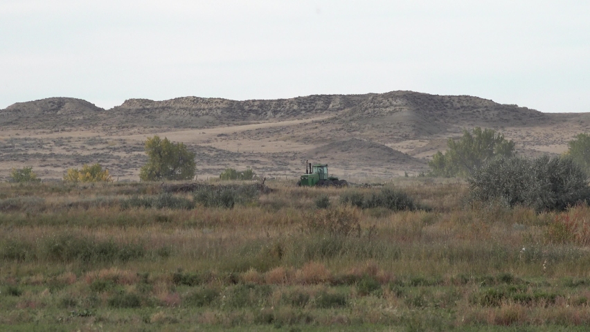 Green Farm Tractor Plowing Field with Mountain Background and Desert Heat Waves