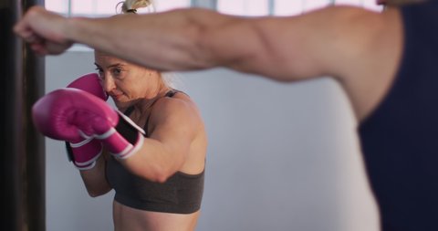 Caucasian female boxer wearing boxing gloves training with punching bag with male trainer at the gym. sports, training and fitness concept