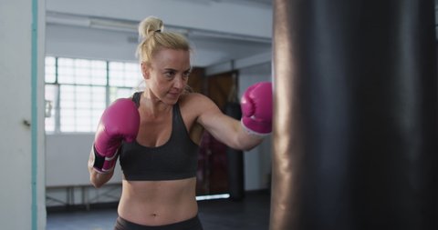 Caucasian female boxer wearing boxing gloves training with punching bag at the gym. sports, training and fitness concept