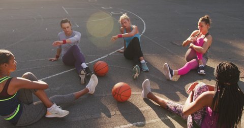 Diverse female basketball team wearing sportswear, stretching. basketball, sports training at an outdoor urban court.