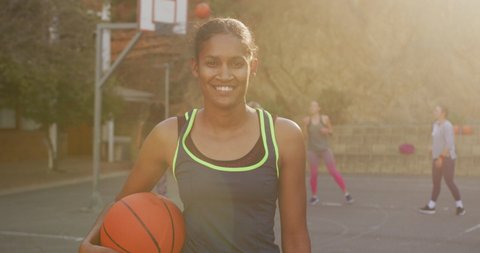 Portrait of african american female basketball player holding ball and looking at camera. basketball, sports training at an outdoor urban court.