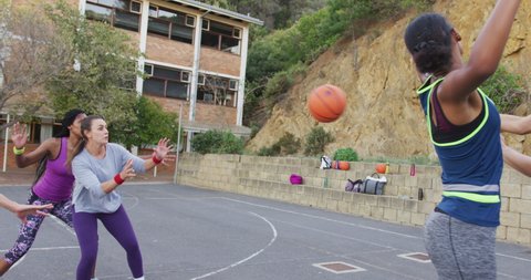 Diverse female basketball team playing match, dribbling and shooting ball. basketball, sports training at an outdoor urban court.