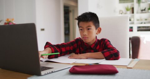 Asian boy at home, sitting at table using laptop for online school lesson. at home in isolation during quarantine lockdown.