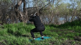  4k video woman doing squat exercise outdoors in headphones