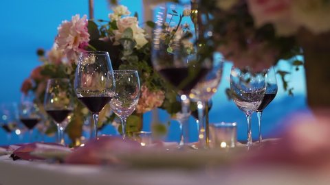 Organize evening event party pink flowers red wine glass wedding reception United States. Close up Wedding decor beach set up candle catering chair dining dinner outside. Dolly shot camera.
