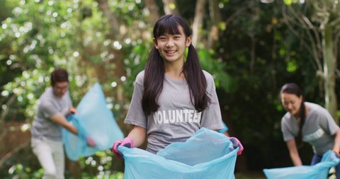 Smiling asian girl wearing volunteer t shirt holding refuse sack for collecting plastic waste. eco conservation volunteers doing countryside clean-up.