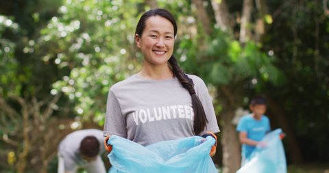 Smiling asian woman wearing volunteer t shirt holding refuse sack for collecting plastic waste. eco conservation volunteers doing countryside clean-up.
