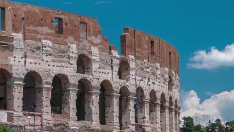 Many tourists visiting The Colosseum or Coliseum timelapse, also known as the Flavian Amphitheatre in Rome, Italy. Traffic on the road and cloudy blue sky