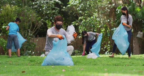 Asian parents, son and daughter wearing face masks holding refuse sacks collecting plastic waste. eco conservation volunteers doing countryside clean-up during coronavirus covid19 pandemic. .