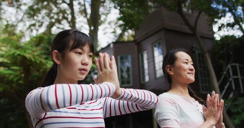 Happy asian mother exercising in garden with daughter, practicing tai chi together. happy family, at home in isolation during quarantine lockdown.