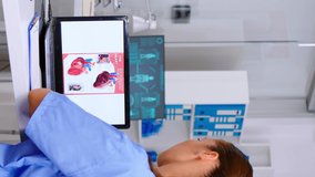 Vertical video: Assistant expertise doctor in medical uniform examining heart disease using laptop, writing on clipboard informations. Physician nurse analysing medicine documents, diagnosis of