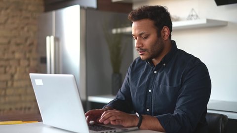 Smart and clever indian male freelancer using laptop computer for work on the distance, focused mixed-race eastern guy is typing, texting, messaging online, working at new project from home