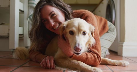 Smiling caucasian woman kissing and cuddling her pet dog sitting on floor at home. lifestyle, pet, companionship and animal friendship concept.