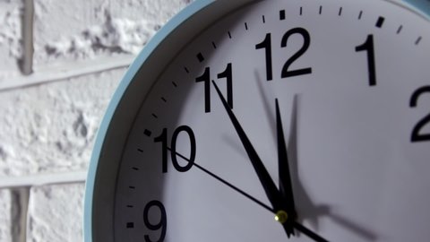 It is five to twelve, the clock is ticking. White Watch shows the time 5 before 12. Close up to a wall clock, with five minutes to twelve o`clock