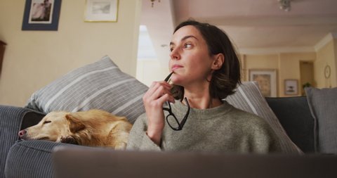 Caucasian woman using laptop working from home with her pet dog next to her on sofa. pet companionship, domestic life and working from home concept.