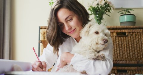 Caucasian woman drawing working from home and cuddling her pet dog. pet companionship, domestic life and working from home concept.