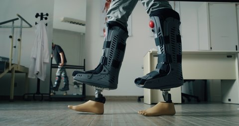 Cinematic shot of young patient with disability is trying to walk for first time with artificial latest innovative futuristic technology bionic legs prosthesis to take first steps in modern clinic.
