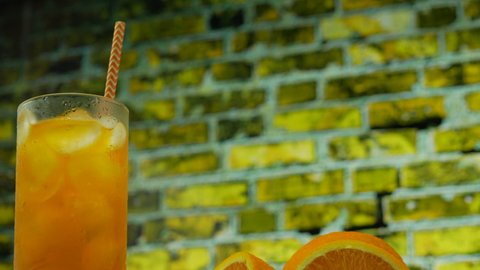 Yellow lemonade with ice in a transparent glass. Orange juice in a glass on the background of a yellow brick wall