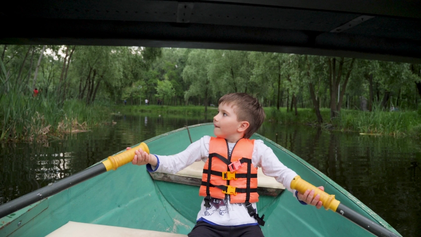 Development child rowing oars on a boat a lake park city. Kid rides a boat with paddle. Recreation children