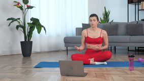 Fit woman in sportswear sits on yoga mat tells talk fitness trainer, study online remote video conference call webcam chat laptop computer, distance sports education lesson course webinar at home