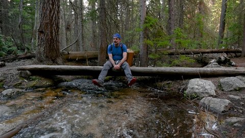 A hiker relaxing on a log bridge over a small creek in the Wild Basin of Rocky Mountain National Park, Colorado, USA